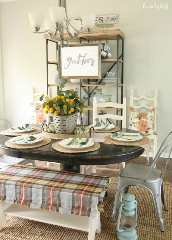 Thanksgiving table set with white chairs and shelving unit behind table.