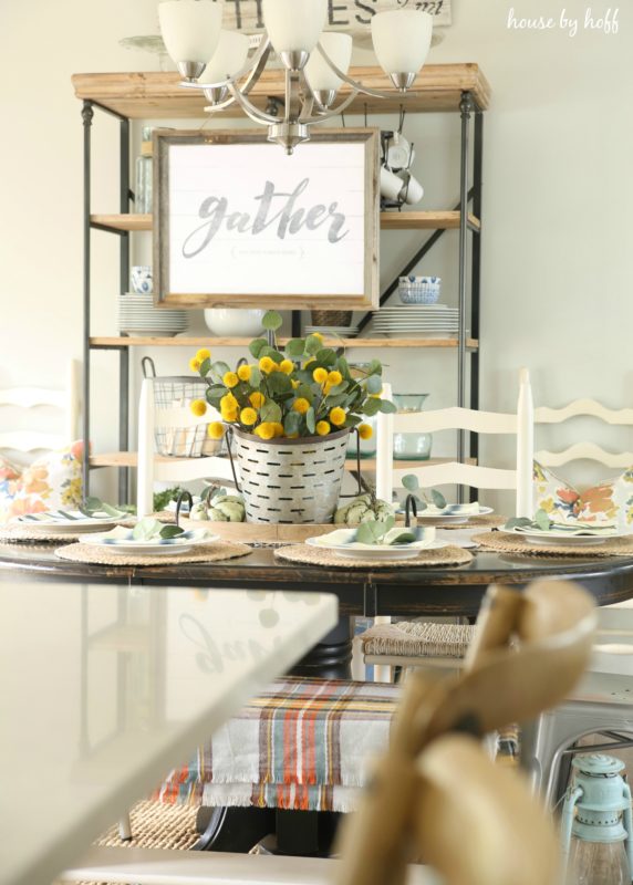 Dining room table decorated with yellow flowers and eucalyptus leaves.