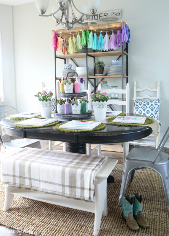 Dining room with artwork on table and boots under the table.