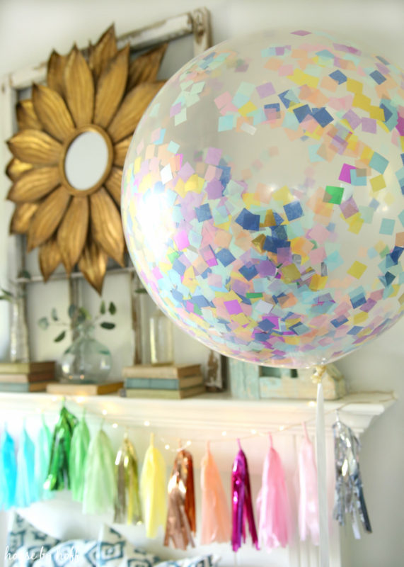 Clear balloon with multi coloured bits of paper inside it hanging by the mantel.