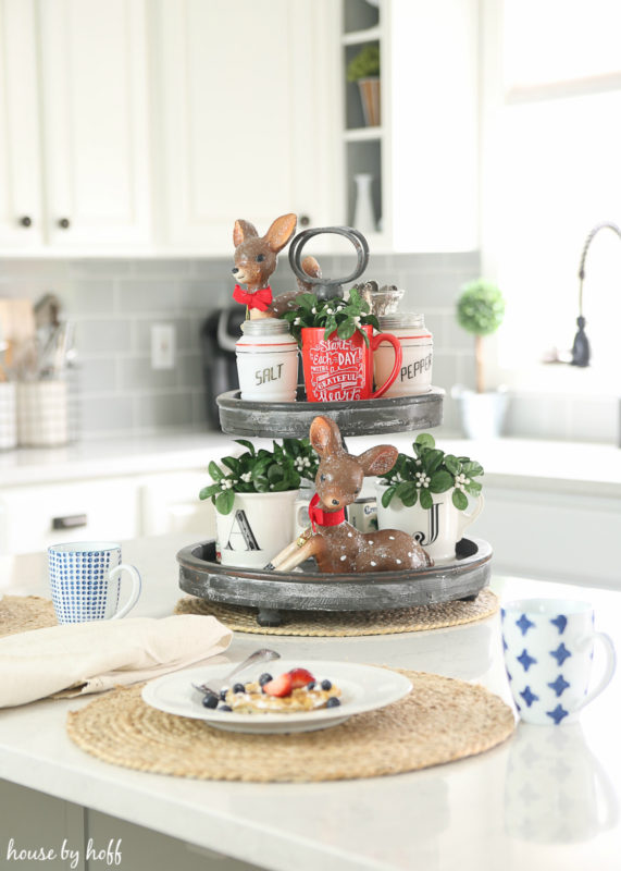 A tiered tray on the kitchen island with little deer figurines and plants on it.