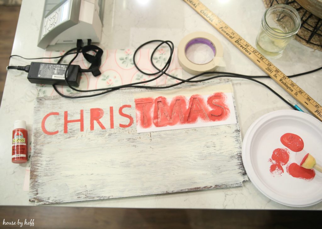 Using a stencil to make the word Christmas on the wooden board.