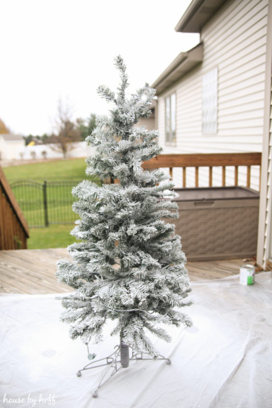 A flocked Christmas tree on the deck of a house outside.