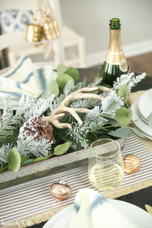 Champagne in a glass, beside gold ornaments and a centrepiece with greenery and antlers.