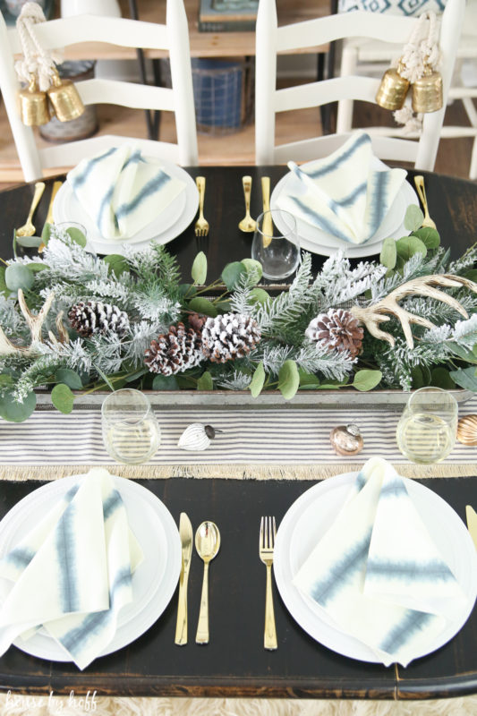 Aerial view of the table with gold cutlery, a green centerpiece, and pine cones.