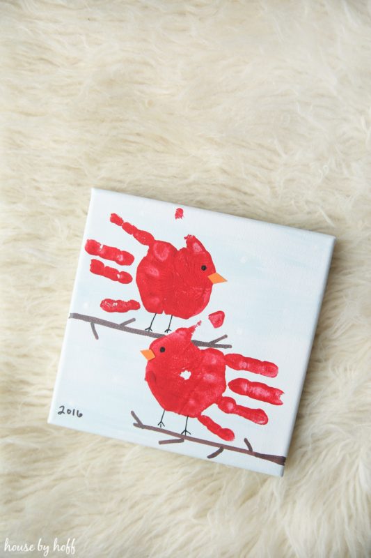 Two little red cardinal birds on a white artists canvas.