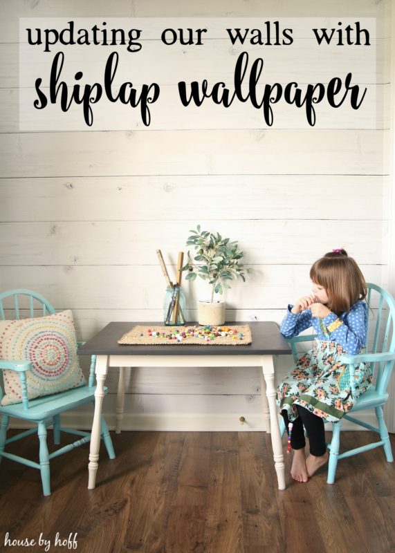 Table and chairs and little girl sitting at table in front of shiplap wall.