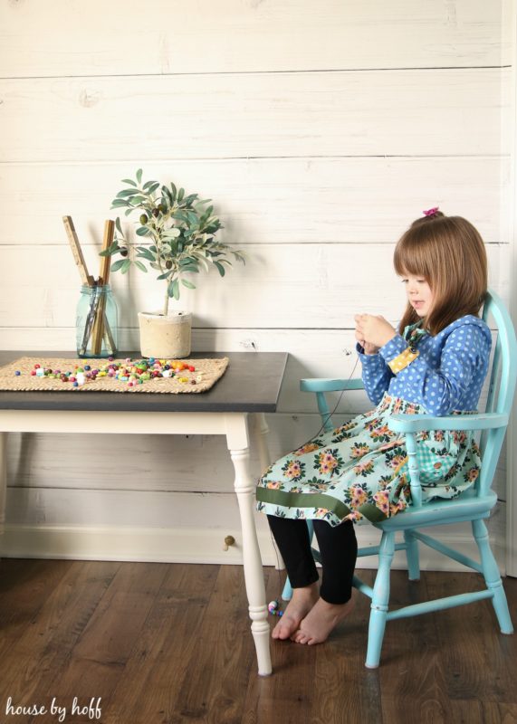 A little girl sitting in her playroom stringing beads.