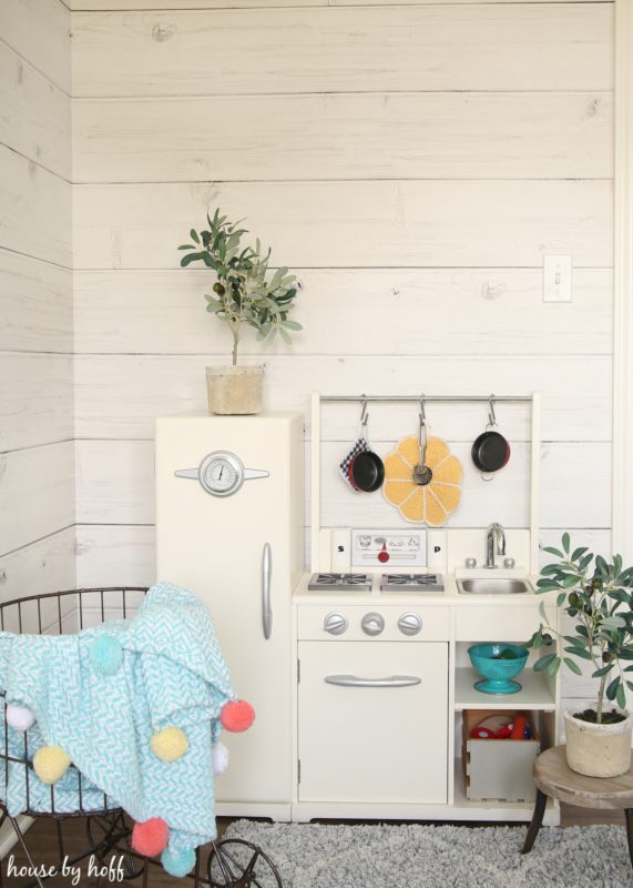 Little play kitchen for a child in front of shiplap wall.