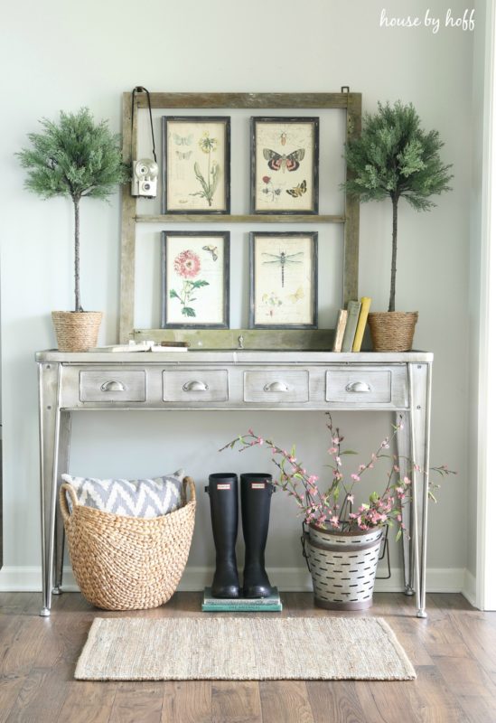 Side hallway table with rubber boots underneath it and a picture frame with art in it on the table.