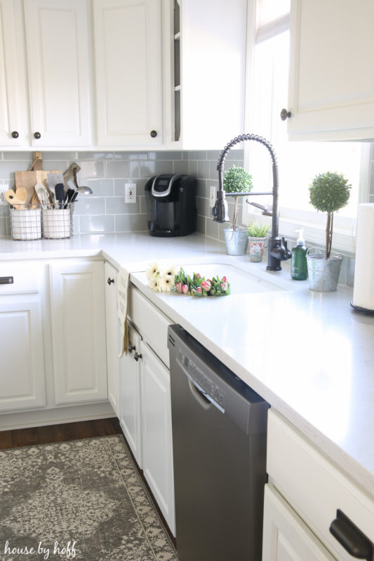 A white kitchen with a sink with flowers in it and a coffee maker in the corner.