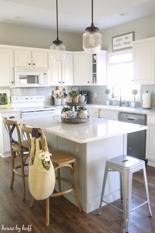 A white kitchen with a white island an a bag with flowers hanging on the back of a chair.