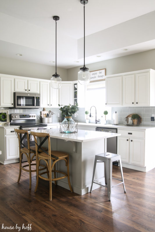 A white kitchen with white cabinets and island and a dark wood laminate floor.