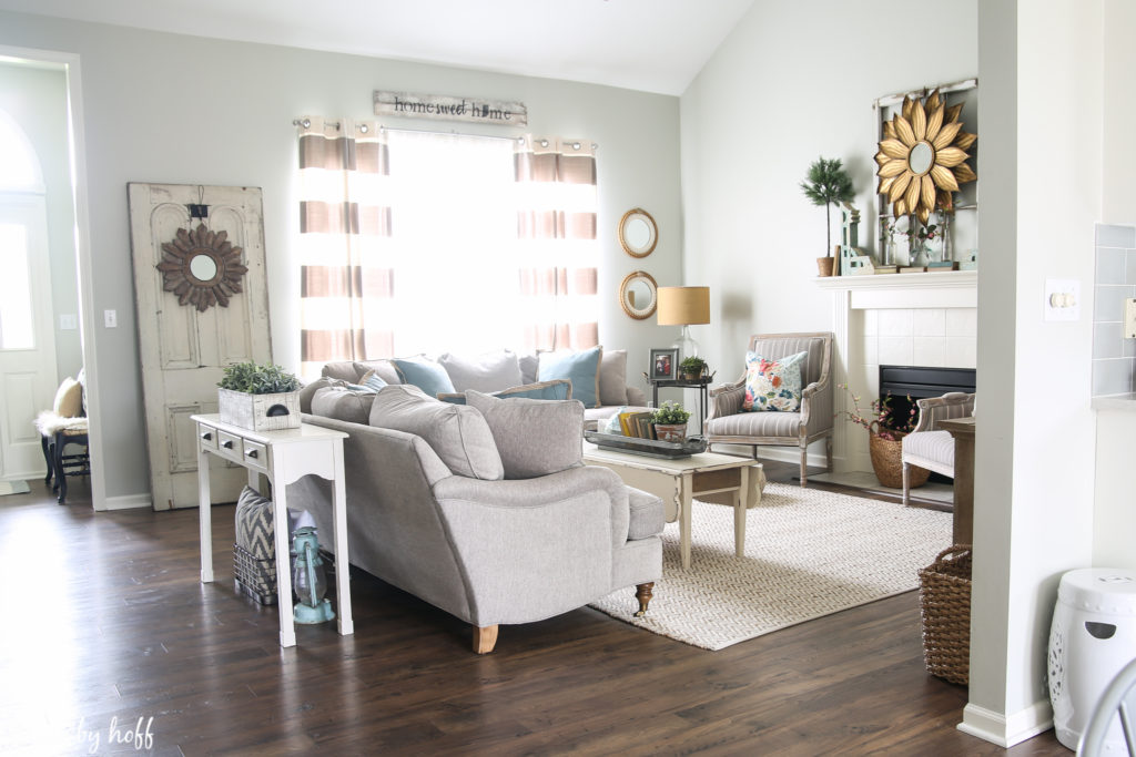 A view of the living room with laminate flooring, neutral couches and area rug.