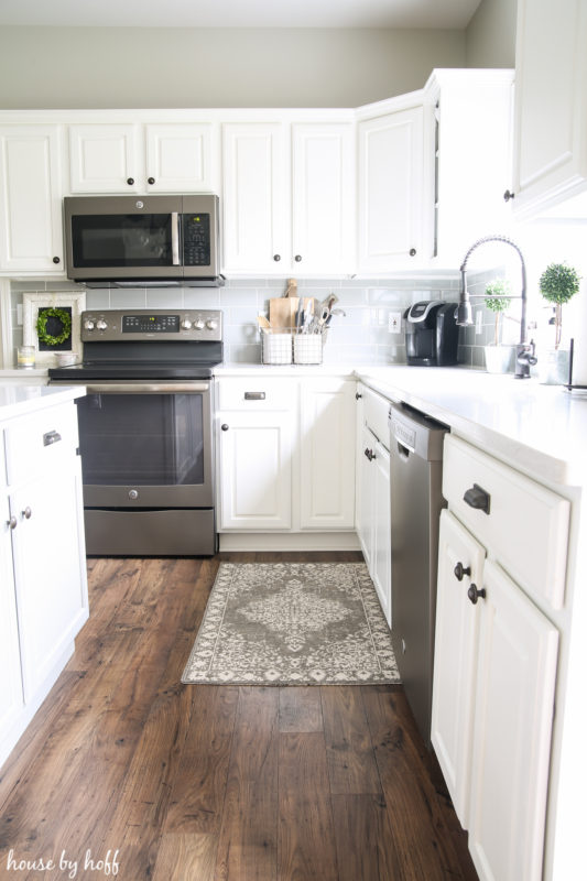 White kitchen cabinets, a small rug by the sink, and stainless steel stove and microwave.