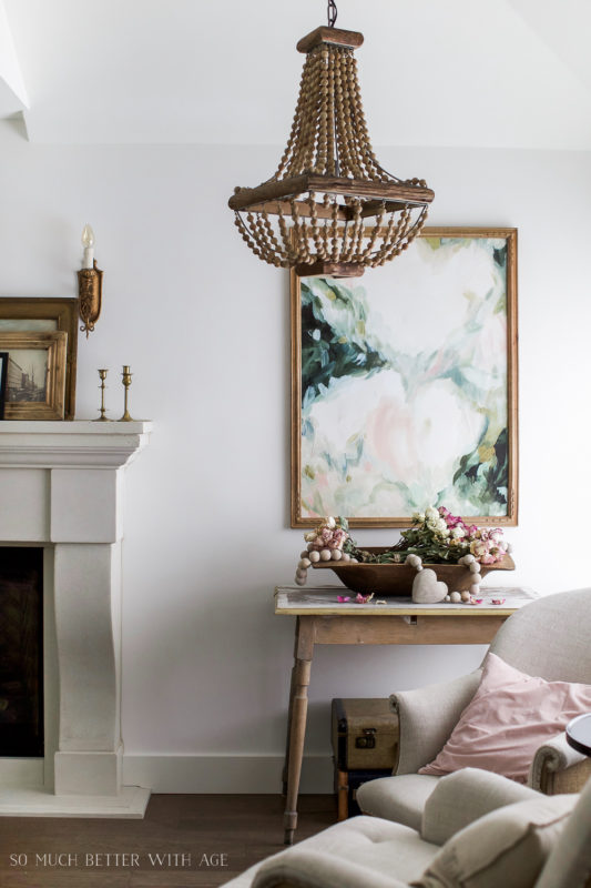 A pink, green and white floral picture in the living room beside a fireplace.