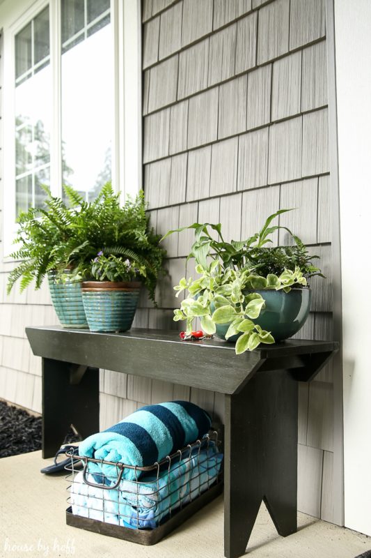 A five board bench with plants on it and towels underneath in a wire basket.