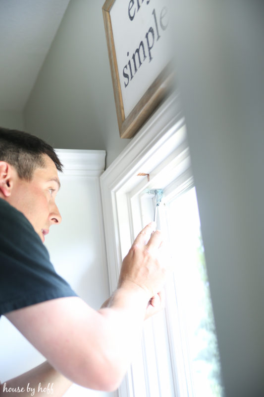 A man installing the blinds in the kitchen.