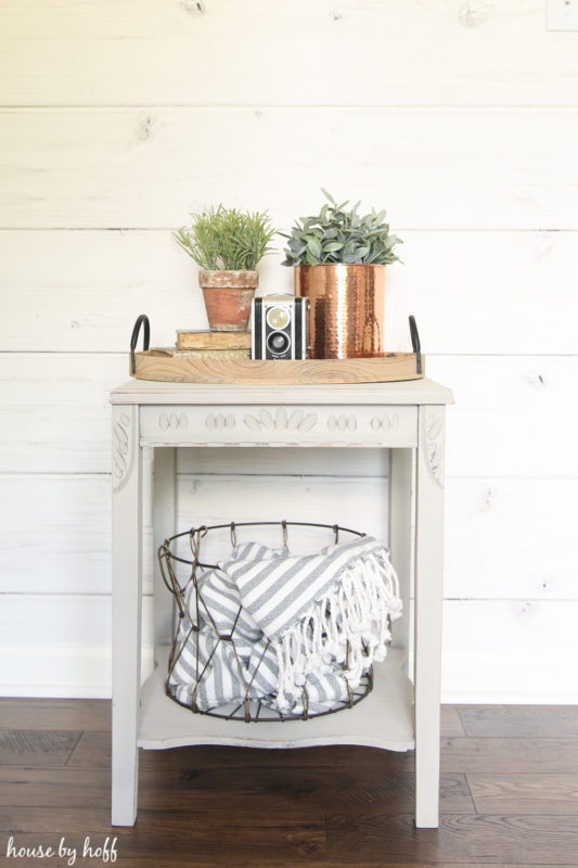 Painted side table with wire basket on bottom shelf and plants on top.