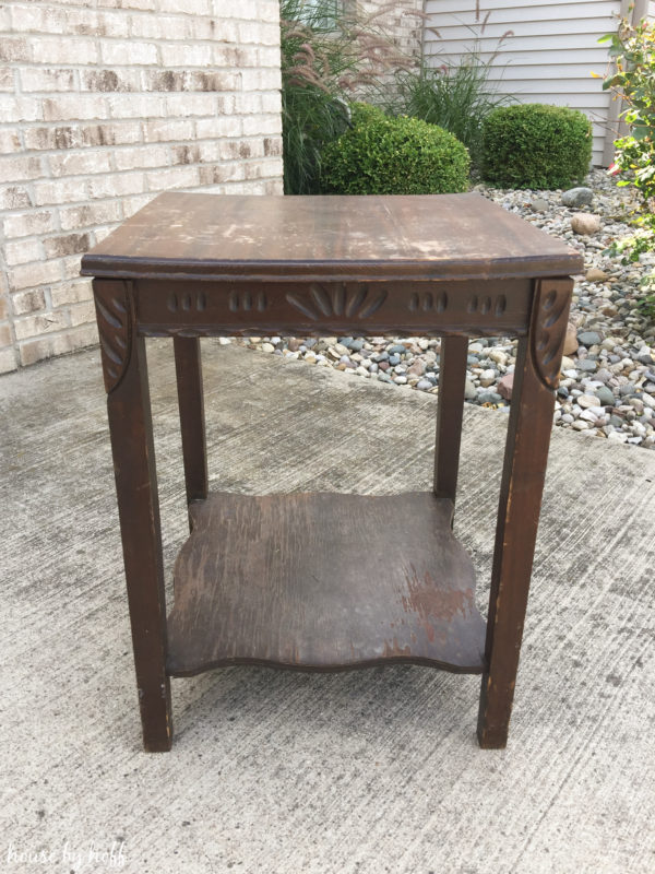 An old brown worn out side table outside in driveway.