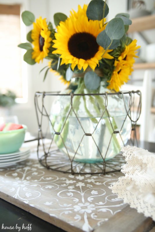 Large yellow sunflowers in vase in a metal wire basket on the tray.