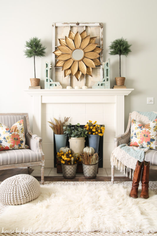 White fireplace mantel with flowered mirror on mantel and flowers in front of the fireplace.