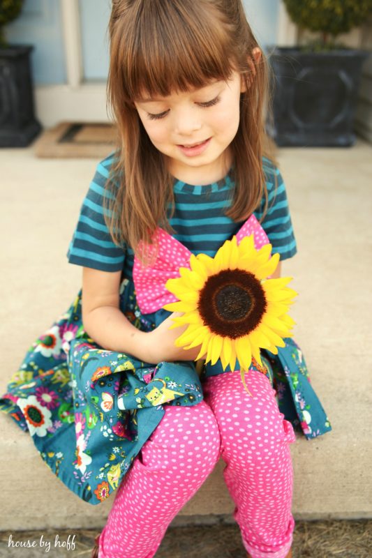 Little girl with a sunflower in her hand wearing pink pants and pink bow.