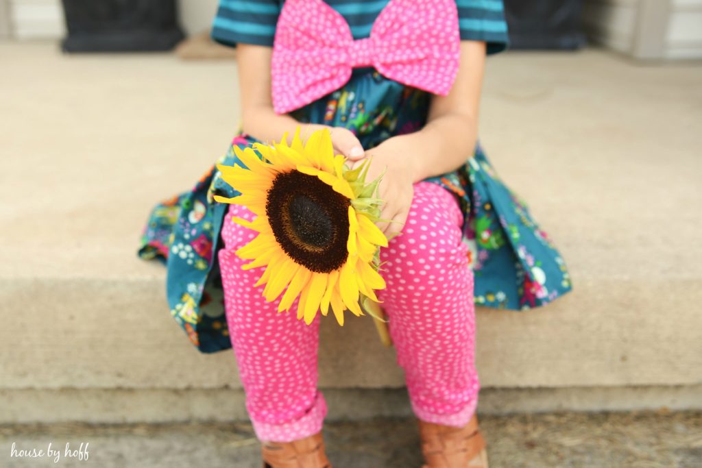 The girl sitting on the front porch steps with a large yellow sunflower in her hand.