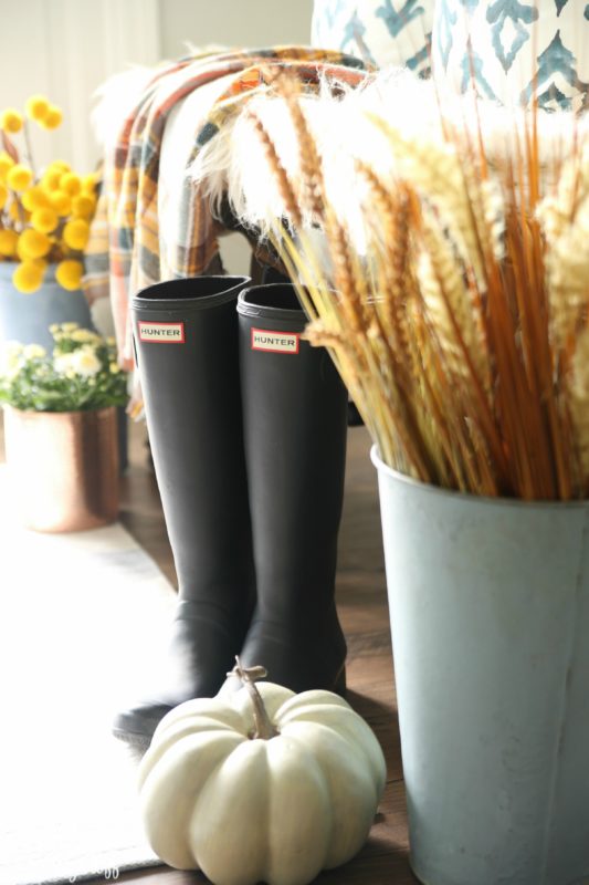 Large planters filled with stalks of wheat and yellow flowers beside the boots and pumpkins.