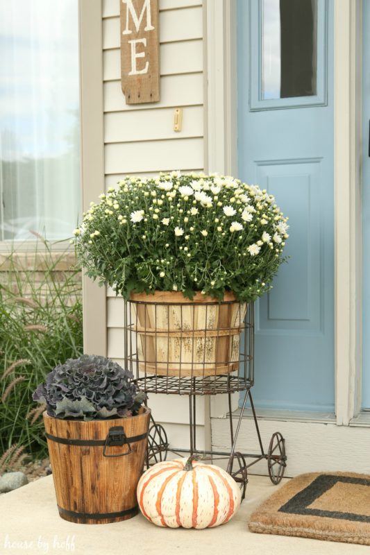 Wire basket on wheels with a large wooden planter in it and white flowers.