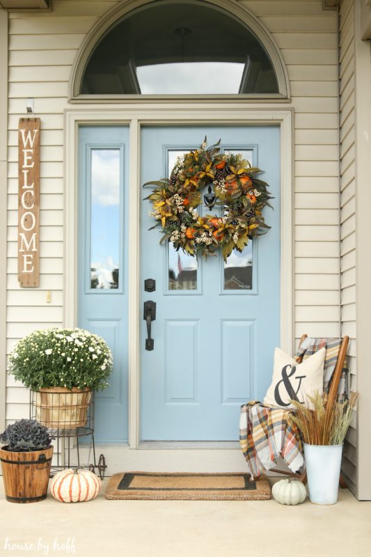 Front door painted light blue with a green, orange and yellow wreath hanging on it.