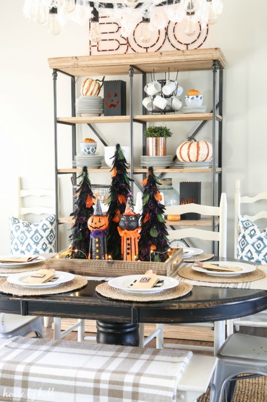 Decorated Halloween table with open shelving unit behind it decorated with pumpkins.