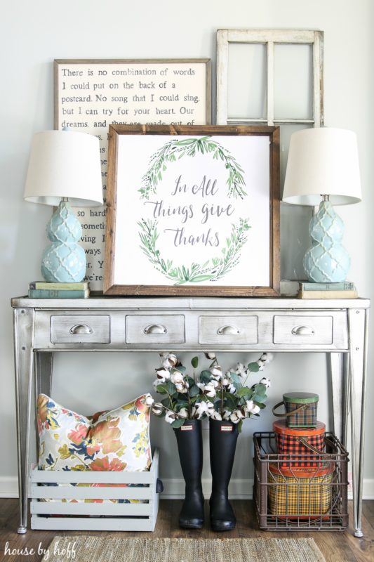 Pewter side table with framed printable on top and two light blue lamps.   