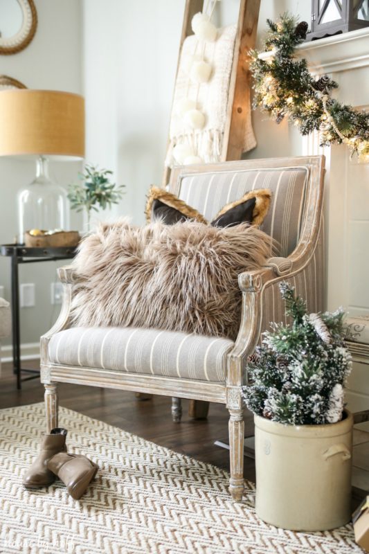 A cozy neutral chair with a fluffy pillow beside the fireplace mantel.