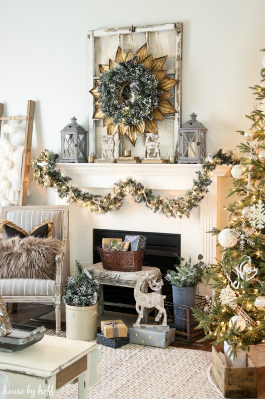 A neutral holiday mantel with a garland hanging on it, a Christmas tree in the corner, and a deer in front of the fireplace.