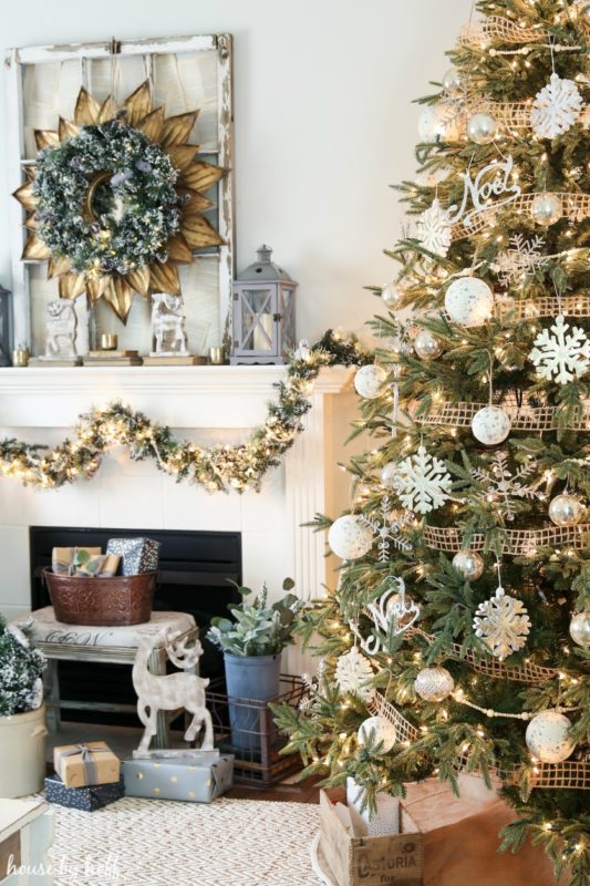 Christmas tree decorated with white neutral ornaments, and white neutral fireplace mantel.