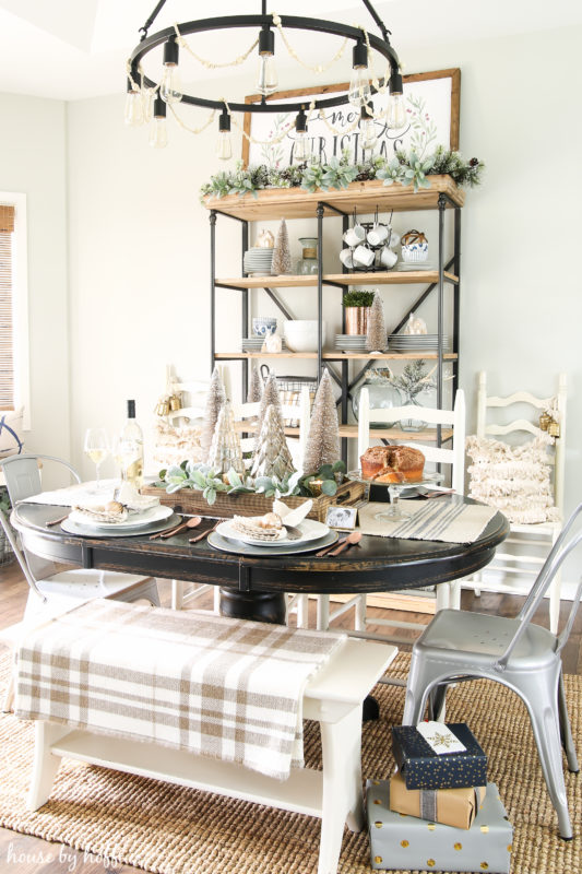 wooden dining room table with wrapped presents beside it, and mini trees on the table.