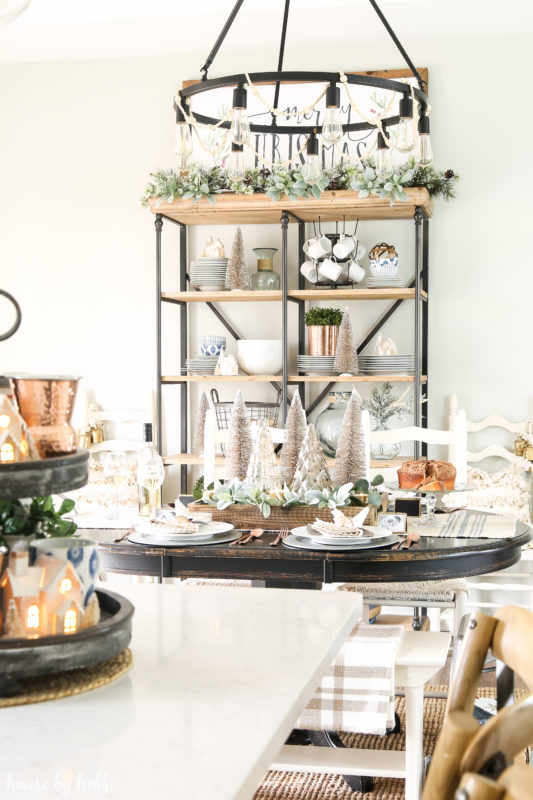 Metal chandelier over the dining room table with open shelving behind it.