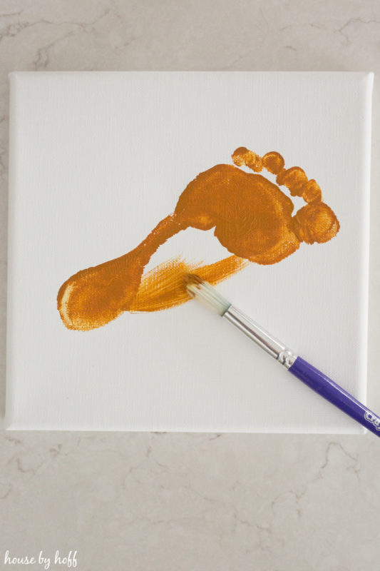 A footprint on a white canvas with a paint brush filling in the spaces.