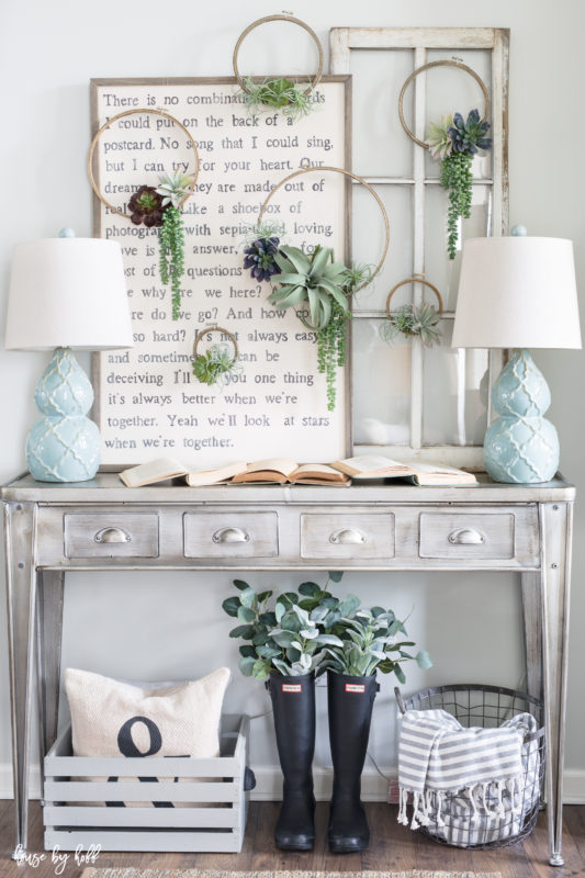 Faux green plant wreaths hanging on wall above table.