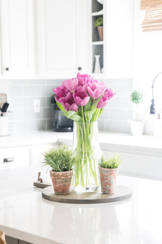Vase with pink tulips and pots of plants in kitchen.