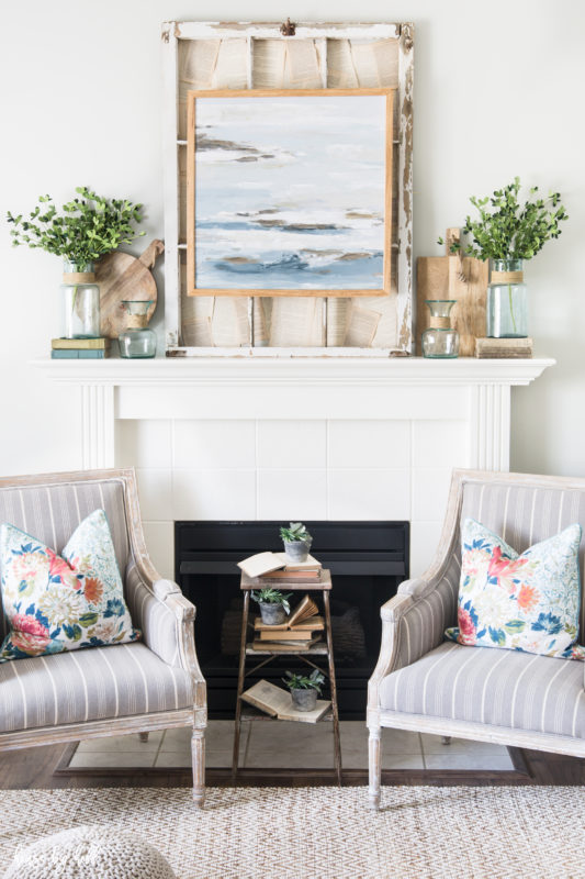 Fireplace mantel with picture on it and two faux green plants on either side.