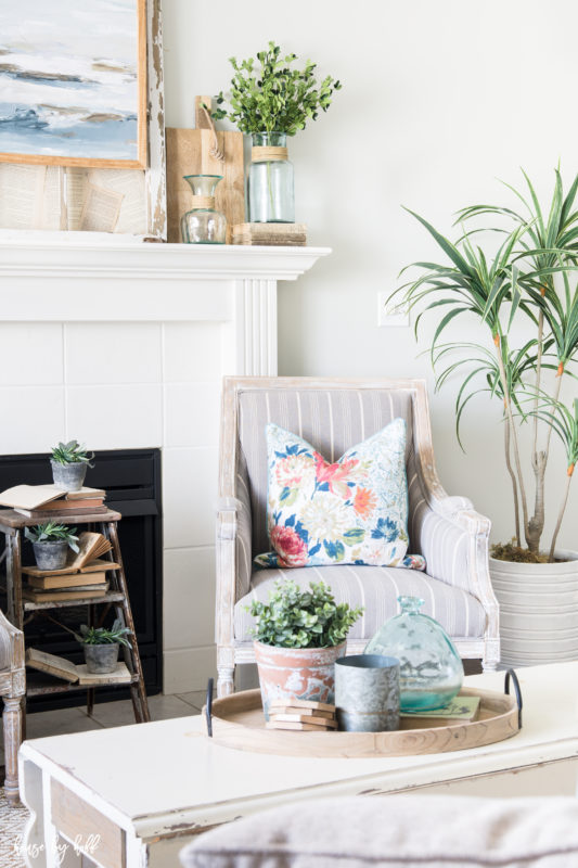 A striped white and gray armchair in front of the fireplace mantel.