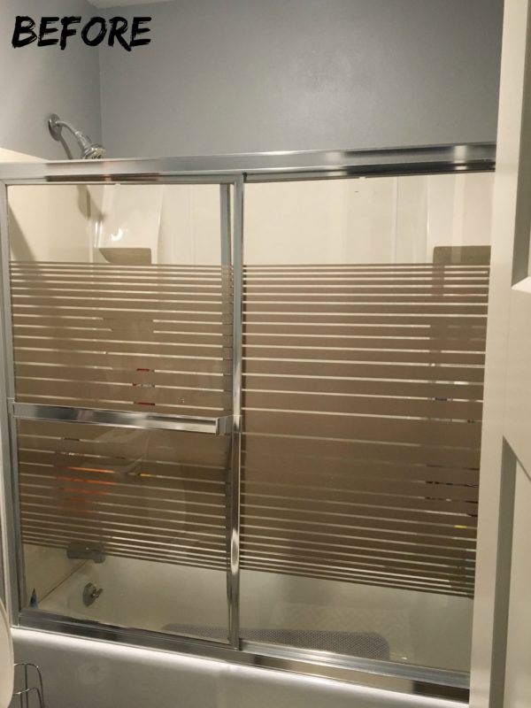 Before picture with a glass shower door with lines on it and gray walls.