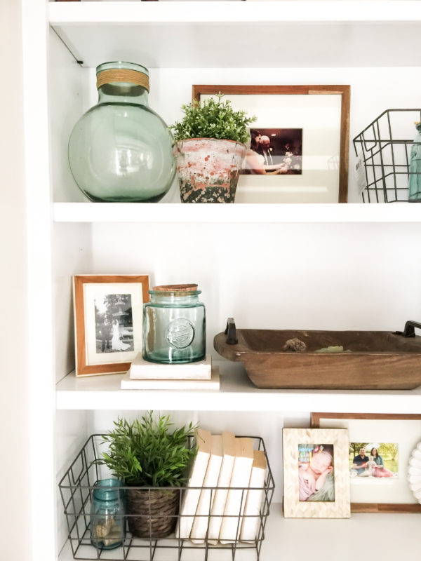 Open white shelves with picture, glass vase and wire baskets.