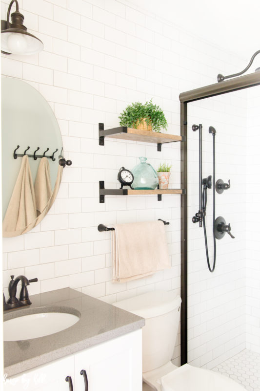 Small bathroom with white subway tile and small shelves on wall.