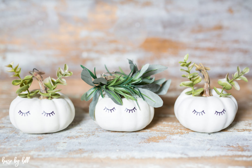 3 little decorated white mini pumpkins on a table.