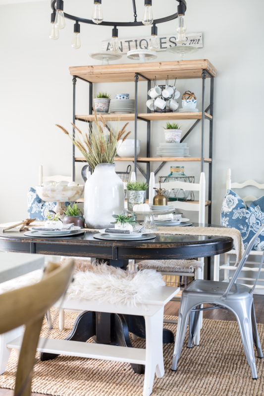 Wooden dining table with white vase filled with wheat and neutral decor.