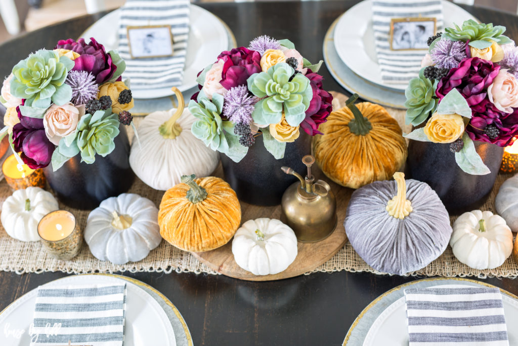 Table runner with colorful flower centrepieces in middle and velvet pumpkins and candles.