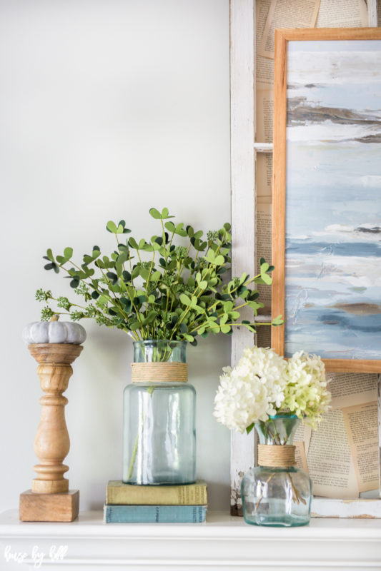 Vases with flowers and leaves and a candelabra on the mantel.